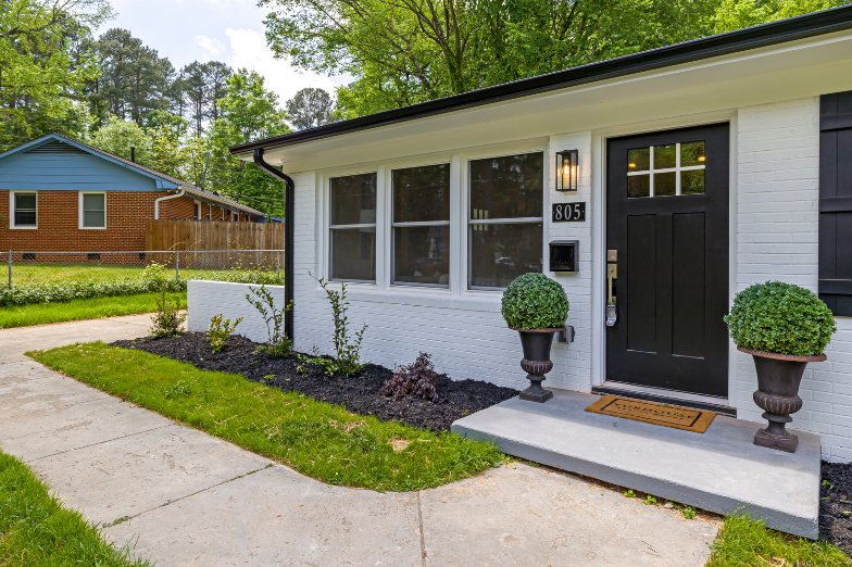 Single-story home with a white brick front and black front door on a sunny day